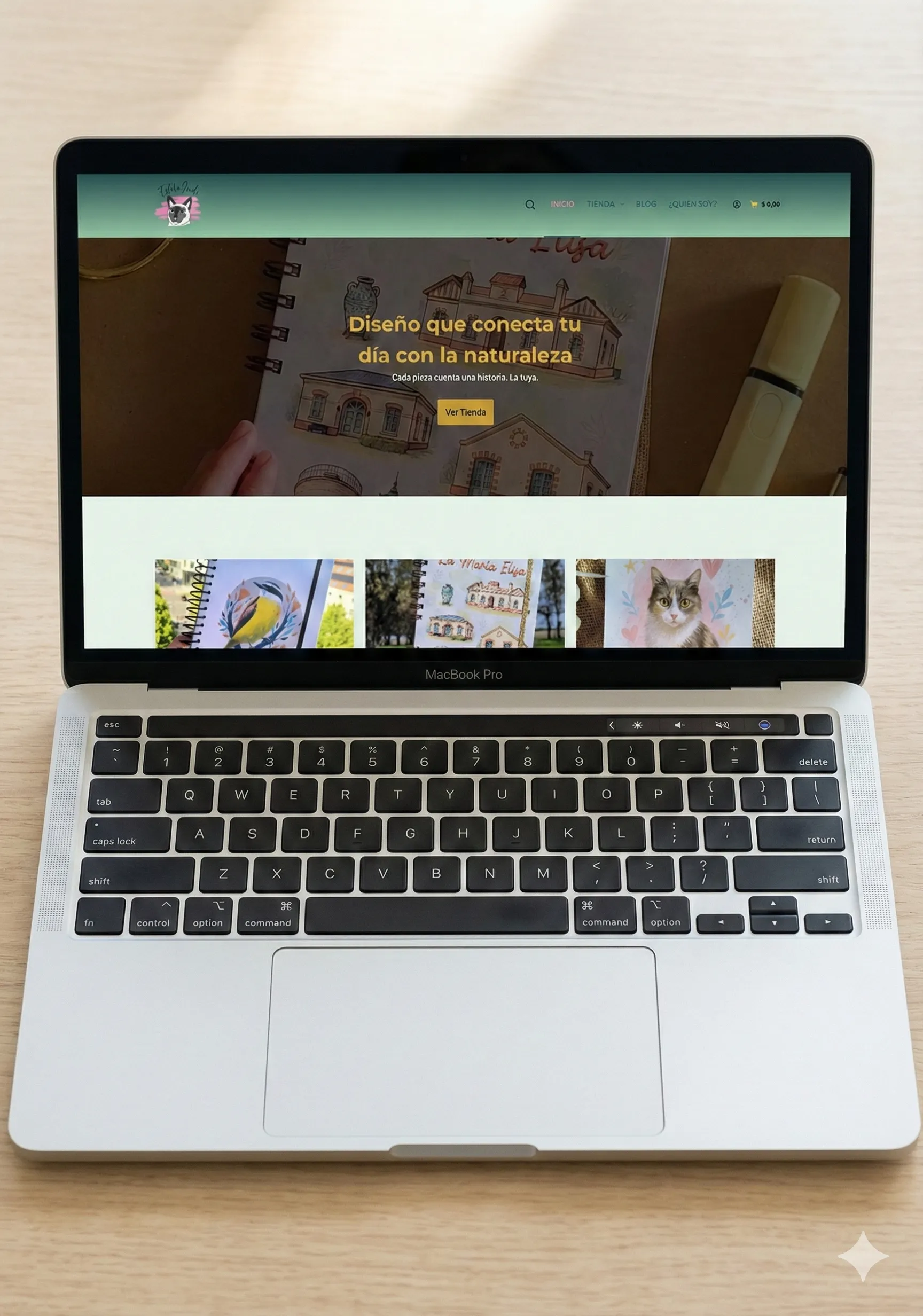 Laptop mostrando la tienda online Estilo Indi con fondo verde pastel, logo de gato ilustrado y catálogo de agendas y cuadernos con diseños de naturaleza.